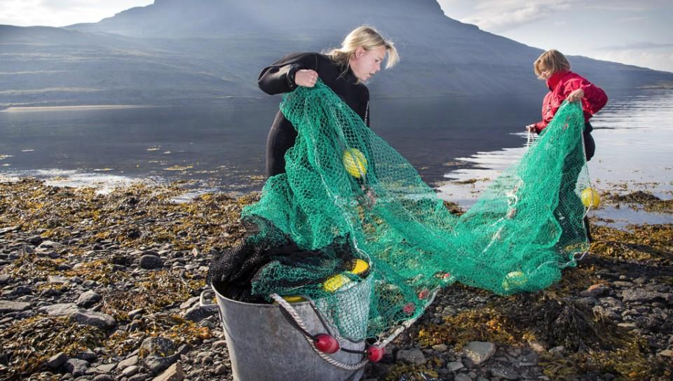 Two students remove a fishing net from the ocean off a rocky coastline